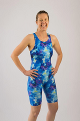 A woman modeling a one-piece athletic swimsuit made in Australia with a blue, purple, and light blue watercolor floral pattern.