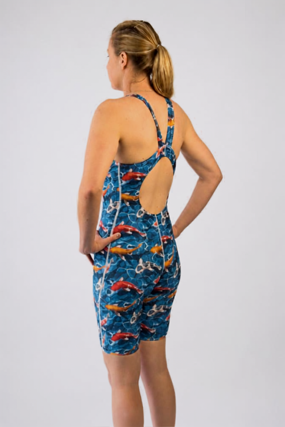 A woman modeling a one-piece athletic swimsuit from the back, featuring a blue background with a pattern of red, orange, fish.